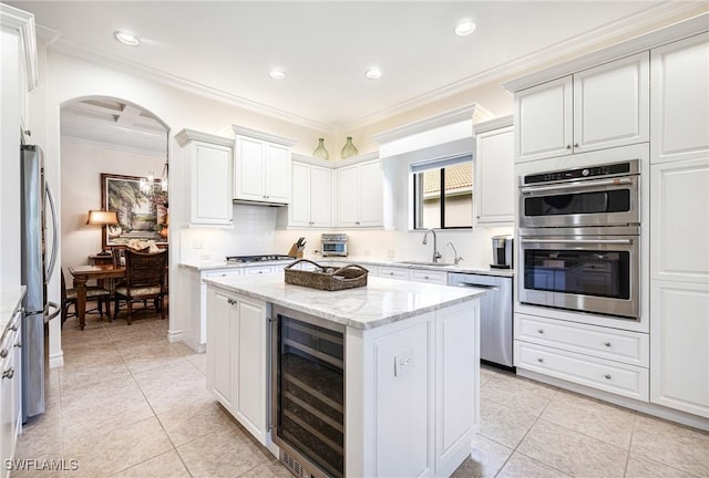 kitchen featuring stainless steel appliances, a kitchen island, beverage cooler, white cabinets, and ornamental molding