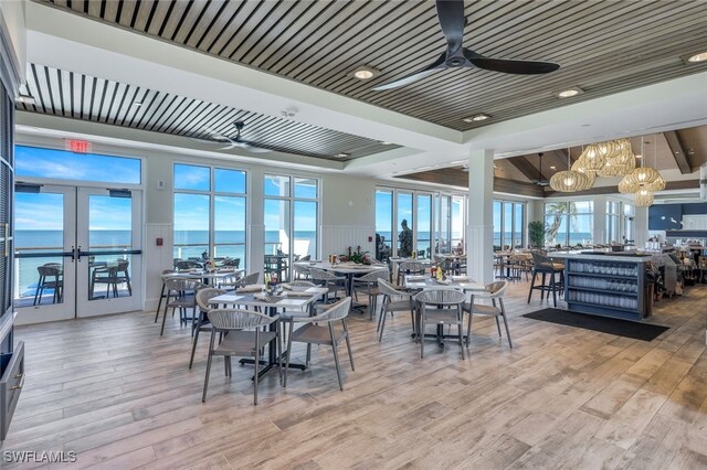 dining room featuring french doors, light hardwood / wood-style floors, wood ceiling, ceiling fan, and a water view