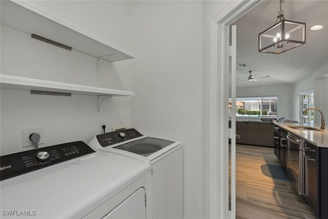 washroom with washer and clothes dryer, sink, ceiling fan with notable chandelier, and wood-type flooring