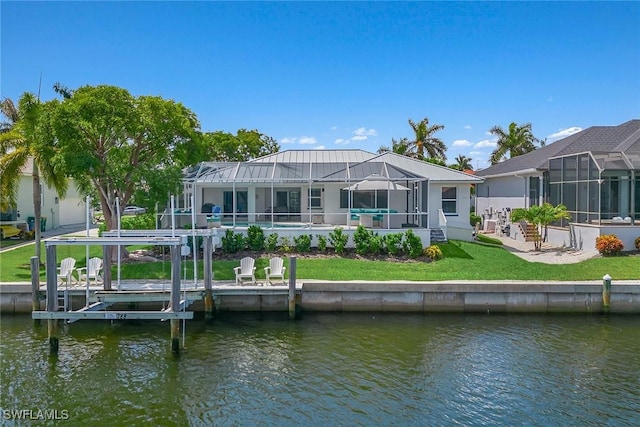 rear view of house with a water view, boat lift, a lanai, and a lawn