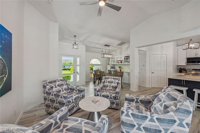 living room with visible vents, light wood-style flooring, a ceiling fan, high vaulted ceiling, and baseboards