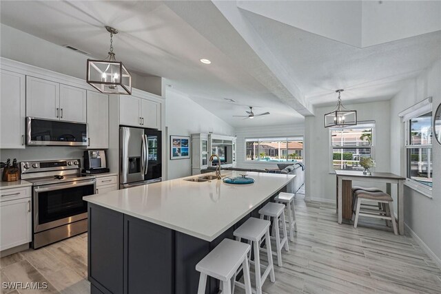 kitchen with ceiling fan with notable chandelier, sink, an island with sink, appliances with stainless steel finishes, and white cabinets