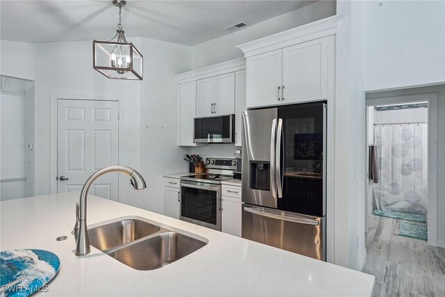 kitchen with a notable chandelier, hanging light fixtures, stainless steel appliances, sink, and white cabinets