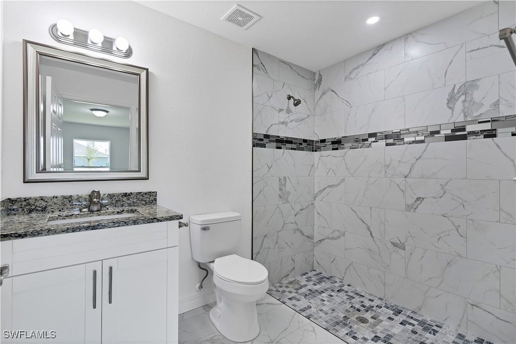 bathroom with a tile shower, vanity, and toilet