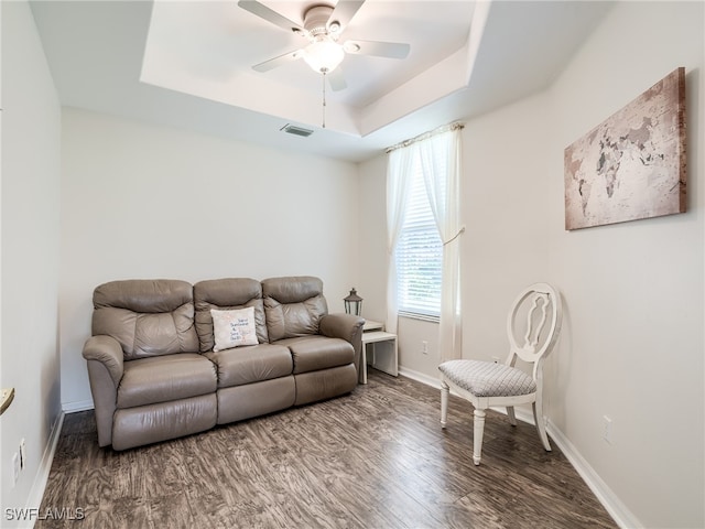 living room with dark wood-type flooring, a tray ceiling, and ceiling fan