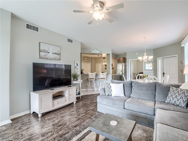 living room with ceiling fan with notable chandelier and dark wood-type flooring