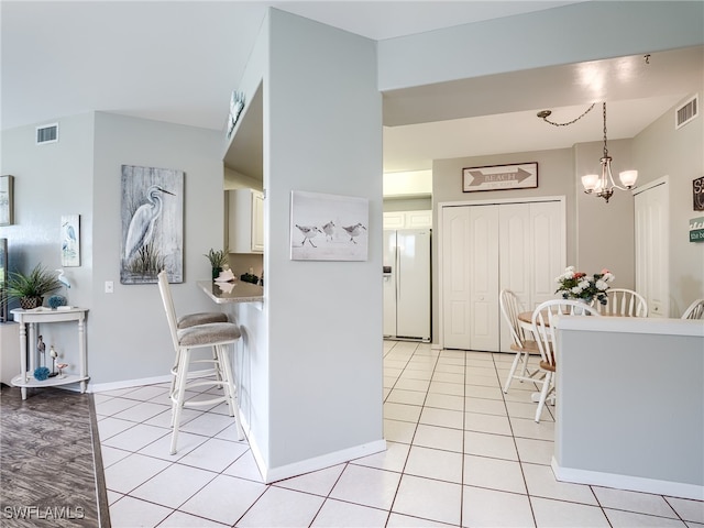 kitchen with white fridge with ice dispenser, a chandelier, light tile patterned floors, decorative light fixtures, and a breakfast bar