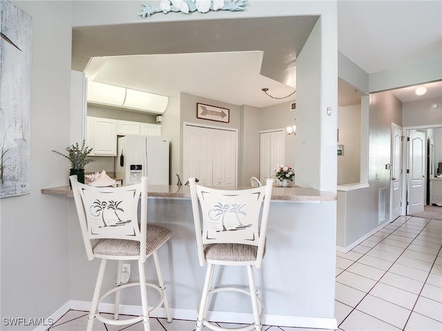 kitchen with a breakfast bar area, light tile patterned floors, kitchen peninsula, white cabinetry, and white fridge with ice dispenser