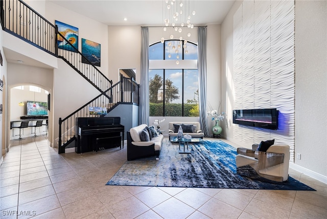 living room featuring a tile fireplace, a high ceiling, light tile patterned floors, and a notable chandelier