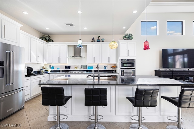 kitchen featuring a breakfast bar area, stainless steel appliances, wall chimney range hood, and an island with sink