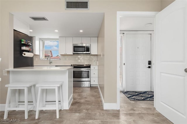 kitchen with white cabinetry, backsplash, kitchen peninsula, stainless steel appliances, and light wood-type flooring