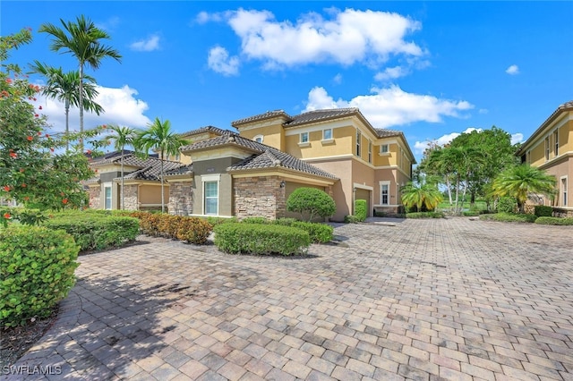 mediterranean / spanish-style home featuring stone siding, a tiled roof, decorative driveway, and stucco siding