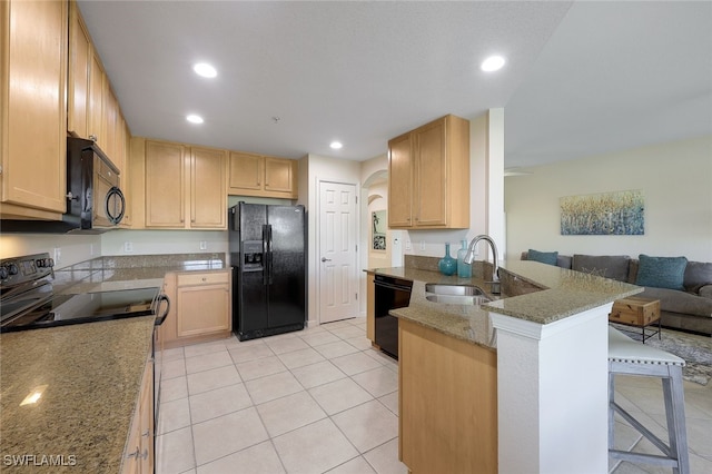 kitchen featuring arched walkways, light brown cabinets, a sink, black appliances, and a kitchen bar