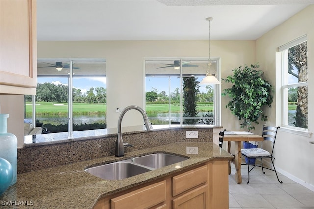 kitchen featuring hanging light fixtures, a ceiling fan, dark stone counters, and a sink