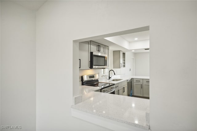 kitchen with gray cabinetry, light stone counters, stainless steel appliances, and sink