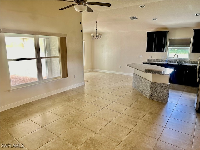 kitchen with light tile patterned floors, a center island, ceiling fan with notable chandelier, stone countertops, and sink