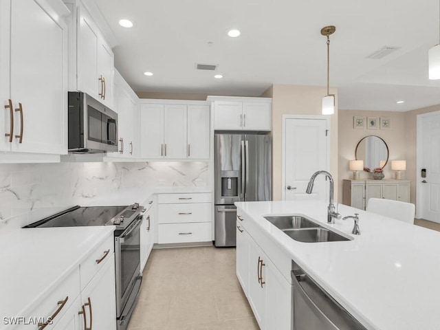 kitchen with pendant lighting, backsplash, white cabinets, sink, and appliances with stainless steel finishes