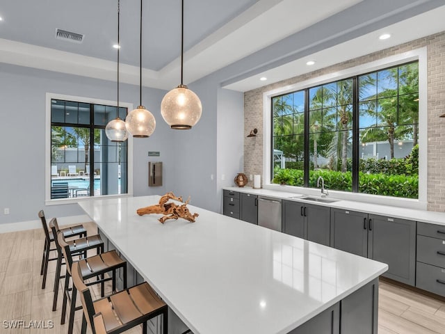 kitchen with pendant lighting, a breakfast bar, a center island, sink, and gray cabinets