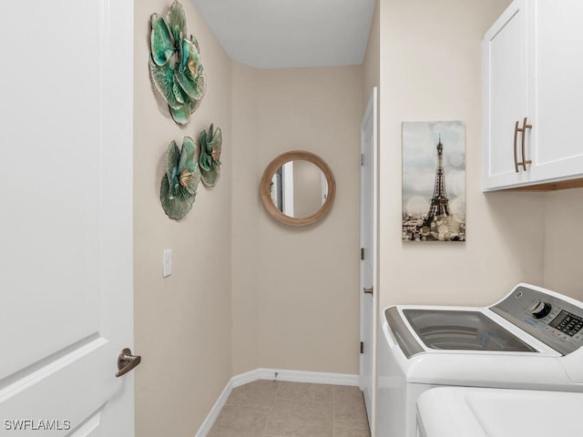 clothes washing area featuring washing machine and clothes dryer, light tile patterned flooring, and cabinets