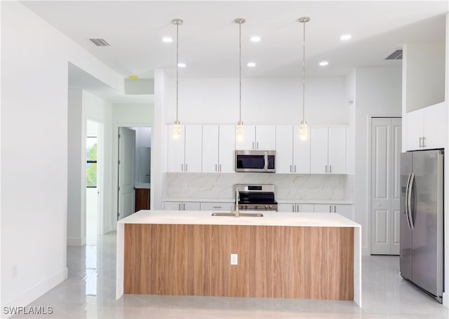 kitchen with a kitchen island with sink, appliances with stainless steel finishes, hanging light fixtures, white cabinets, and backsplash