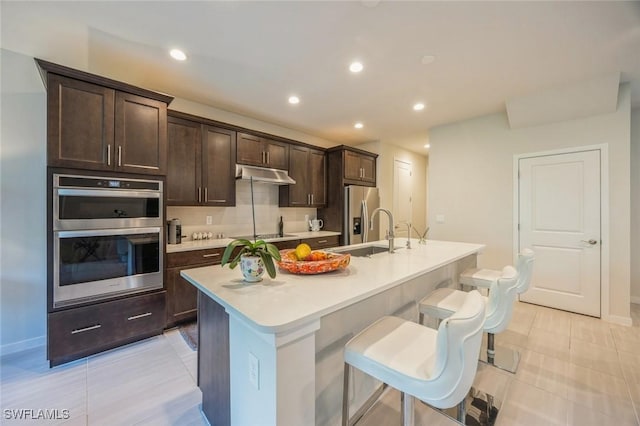 kitchen featuring a kitchen island with sink, under cabinet range hood, light countertops, stainless steel appliances, and a sink