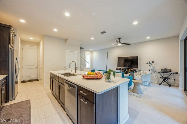 kitchen featuring a center island with sink, a sink, appliances with stainless steel finishes, light countertops, and dark brown cabinets