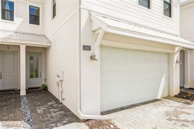 property entrance featuring stucco siding, metal roof, decorative driveway, an attached garage, and a standing seam roof