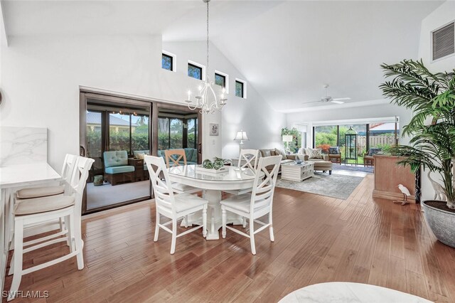 dining area with ceiling fan with notable chandelier, high vaulted ceiling, wood finished floors, and visible vents