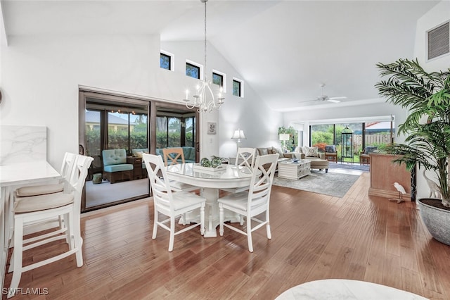 dining space featuring ceiling fan with notable chandelier, wood finished floors, visible vents, and high vaulted ceiling