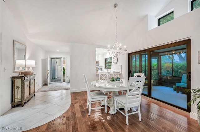 dining room with a towering ceiling, an inviting chandelier, baseboards, and wood finished floors