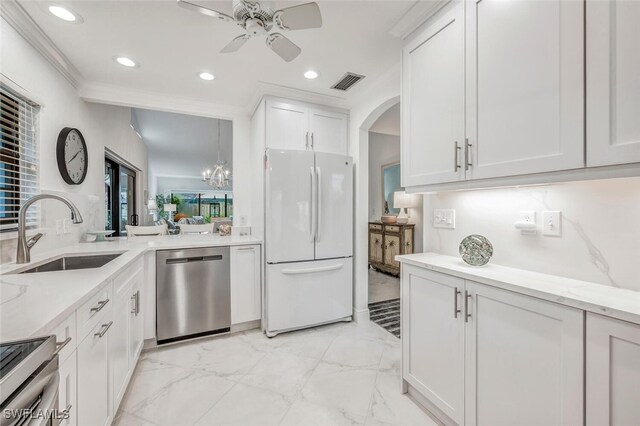 kitchen with ceiling fan with notable chandelier, sink, stainless steel appliances, ornamental molding, and white cabinetry