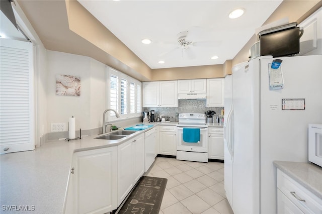 kitchen with a sink, under cabinet range hood, backsplash, white cabinetry, and white appliances