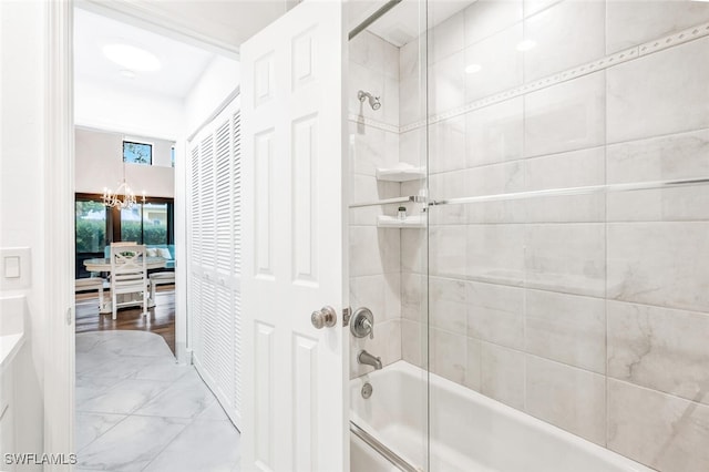 full bathroom with a notable chandelier, marble finish floor, and bath / shower combo with glass door