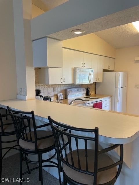 kitchen featuring white cabinetry, white appliances, backsplash, a kitchen breakfast bar, and vaulted ceiling