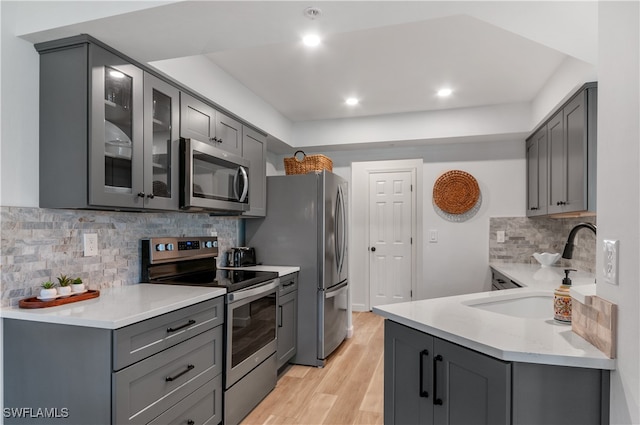 kitchen with gray cabinets, tasteful backsplash, stainless steel appliances, sink, and light hardwood / wood-style floors