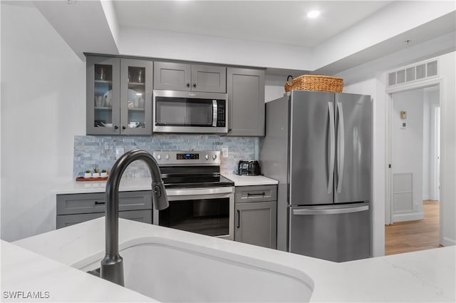 kitchen featuring backsplash, hardwood / wood-style flooring, appliances with stainless steel finishes, light stone counters, and gray cabinets