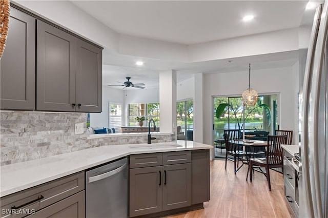 kitchen with stainless steel appliances, sink, decorative backsplash, ceiling fan, and light wood-type flooring