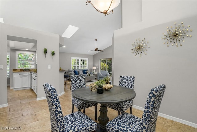 dining area with lofted ceiling with skylight, stone finish flooring, ceiling fan, and baseboards