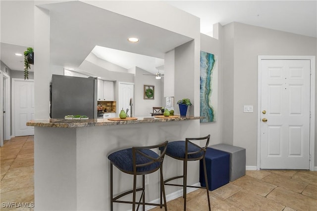 kitchen with freestanding refrigerator, a peninsula, vaulted ceiling, stone counters, and a kitchen bar