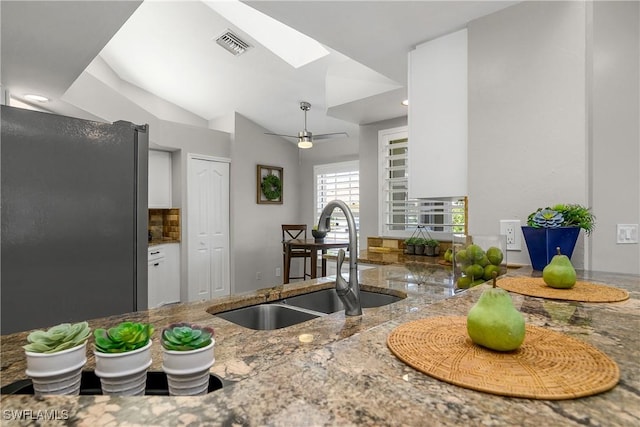 kitchen with vaulted ceiling with skylight, stone countertops, visible vents, freestanding refrigerator, and a sink