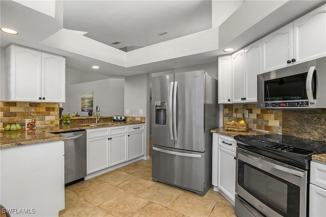 kitchen with white cabinets, a raised ceiling, appliances with stainless steel finishes, dark stone countertops, and a sink