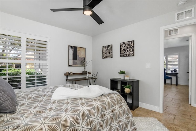 bedroom featuring a ceiling fan, stone tile flooring, visible vents, and baseboards