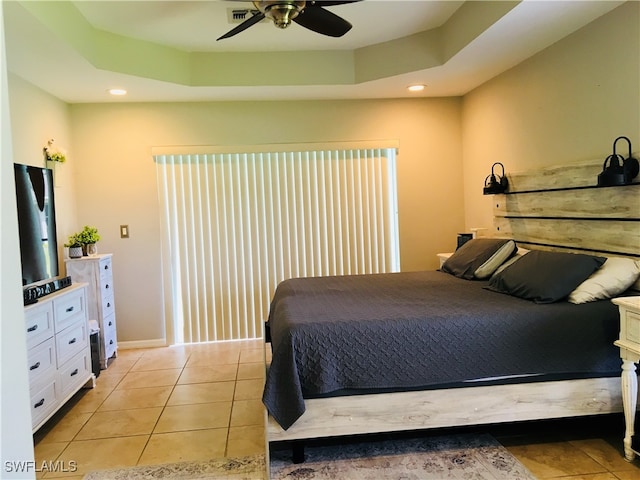 bedroom with a raised ceiling, black refrigerator, light tile patterned floors, and ceiling fan