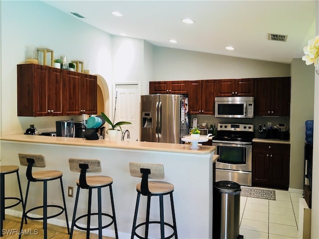 kitchen with a kitchen bar, stainless steel appliances, kitchen peninsula, vaulted ceiling, and light tile patterned flooring