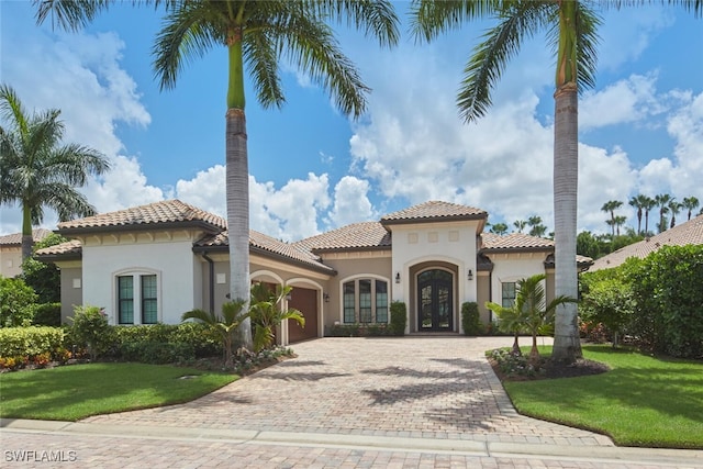 mediterranean / spanish home with an attached garage, french doors, decorative driveway, stucco siding, and a front lawn