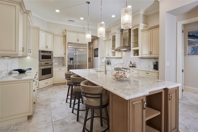 kitchen featuring wall chimney exhaust hood, appliances with stainless steel finishes, light stone countertops, and an island with sink