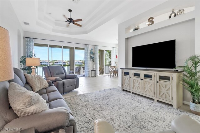 tiled living room with a raised ceiling and ceiling fan