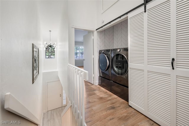 laundry room with washing machine and clothes dryer, an inviting chandelier, a barn door, wood finished floors, and laundry area