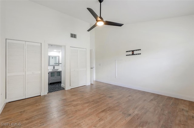 unfurnished bedroom featuring multiple closets, visible vents, high vaulted ceiling, light wood-type flooring, and baseboards