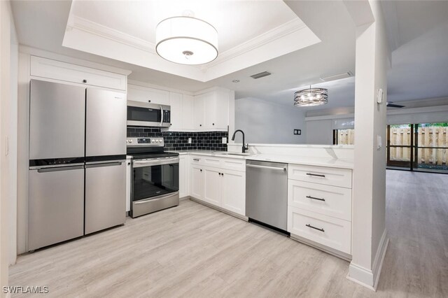 kitchen featuring light hardwood / wood-style floors, white cabinetry, appliances with stainless steel finishes, and a tray ceiling